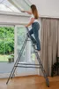 A woman is cleaning a skylight while standing on a stepladder indoors. Podgląd zdjęcia produktu