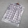 A plaid shirt inside a clear plastic garment bag, lying on a grey carpeted surface. Anteprima dell’immagine prodotto