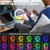 A person is using a smartphone while sitting next to a desk with a laptop and a multi-functional LED lamp that also functions as a wireless charger and alarm clock. Produktbild-Vorschau