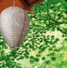 A wasp nest decoy hanging from a wooden overhang, with green foliage in the background. Produktbild-Vorschau
