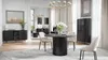 A modern dining room with a round black dining table, chairs, a sideboard, and a display cabinet. Produktbild-Vorschau