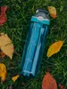 A blue Contigo water bottle is placed on green grass surrounded by fallen autumn leaves. Anteprima dell’immagine prodotto
