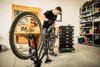 A man is working on a bicycle in a workshop, with storage units and shelves in the background. Náhled obrázku produktu