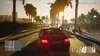 A screenshot from a video game, showing a car driving down a street lined with palm trees during sunset. Produktbild-Vorschau