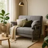 A cozy living room scene with a gray sofa bed, decorative pillows, a blanket, a plant, and a small coffee table. Produktbild-Vorschau