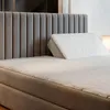 A close-up view of a bed with a gray headboard and a white wedge pillow. Produktbild-Vorschau