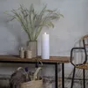 A white LED candle sits on a wooden shelf next to a vase of dried grass and two glasses. Produktbild-Vorschau
