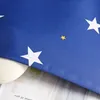 A close-up view of a blue curtain with white and yellow stars, partially covering a white textured object and some text on paper. Produktbild-Vorschau