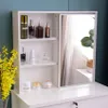 A white vanity with a sliding mirror and various cosmetic products displayed on shelves and the countertop. Voir les images du produit