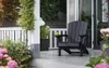 A dark gray Adirondack chair sits on a porch next to potted plants and a railing. Produktbild-Vorschau