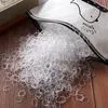 A pile of small, clear, elastic hair ties spilling out of a white bag onto a wooden surface. Anteprima dell’immagine prodotto