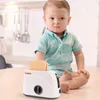 A baby sits on a table next to a toy toaster with pop-up toasts. Anteprima dell’immagine prodotto