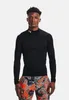 A man wearing a black long-sleeved shirt and patterned shorts against a white background. Produktbild-Vorschau