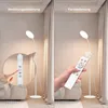 A split image showing a white LED floor lamp. The left side demonstrates touch control with a finger pointing to a control panel on the lamp pole. The right side shows a hand holding a remote control near the lamp, indicating remote control functionality. Produktbild-Vorschau