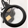 A close-up view of a black magnifying lamp with a sponge and soldering iron visible underneath. Produktbild-Vorschau