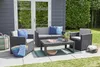 Outdoor patio furniture set with a coffee table, sofa, and armchair, placed on a patio next to a dark gray shed and green hedge. Anteprima dell’immagine prodotto