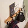 A wooden coat rack mounted on a wall, with two decorative signs, a black cap, and a plaid scarf hanging on it. Voir les images du produit