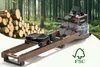 A rowing machine is placed in front of a forest background with a pile of logs on the left and an FSC logo on the right. Produktbild-Vorschau