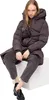 A woman sitting on a white cube, wearing a puffer coat and pants. Produktbild-Vorschau