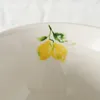 A close-up of a white ceramic bowl with a painted lemon motif. Anteprima dell’immagine prodotto