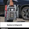 A person is holding a portable jump starter next to a car. Produktbild-Vorschau