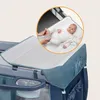 A baby is being changed on a portable changing pad attached to a baby crib/playpen. Produktbild-Vorschau