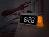 A person reaching for a digital alarm clock on a nightstand. Produktbild-Vorschau