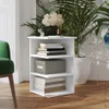 A white corner shelf unit with books and a decorative box on it, placed next to a green chair and large potted plants. Voir les images du produit