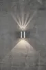 A silver cylinder-shaped LED wall light is mounted on a textured gray concrete wall, casting light upwards and downwards in fan-like patterns. Anteprima dell’immagine prodotto
