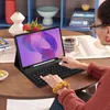 A person is using a tablet with a keyboard case on a wooden table. Produktbild-Vorschau