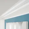 A close-up view of white crown molding against a blue wall. Produktbild-Vorschau