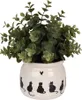 A potted plant with green leaves sits in a beige ceramic pot decorated with black cat silhouettes. Podgląd zdjęcia produktu