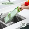 A hand is holding a green mandoline slicer under running water in a kitchen sink. Produktbild-Vorschau