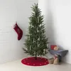 A Christmas tree decorated with white candle lights, a red stocking, and gifts at its base, set against a white wooden wall. Podgląd zdjęcia produktu