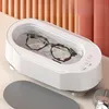 A white ultrasonic cleaner with glasses inside, placed on a table with a minimalist background. Produktbild-Vorschau