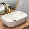 A marble-patterned sink with a gold faucet is shown on a wooden surface, with a gold-rimmed mirror in the background. Náhľad obrázku produktu