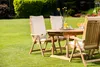 A wooden garden table and chairs set with cushions, set up on a lush green lawn with drinks and flowers on the table. Produktbild-Vorschau