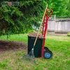 A garden scene with gardening tools and a wheelbarrow filled with mulch. Anteprima dell’immagine prodotto