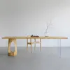 A modern wooden dining table with unique carved legs and clear acrylic legs, set against a plain wall. Produktbild-Vorschau
