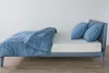 A side view of a bed with blue bedding and pillows against a white wall. Produktbild-Vorschau