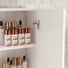 A close-up view of a white bathroom cabinet with several cosmetic bottles on shelves. Náhľad obrázku produktu