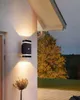 An outdoor wall light illuminates a wall and a small plant at dusk. Produktbild-Vorschau