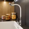 A modern kitchen sink area with a white sink, a flexible white faucet, and glass jars filled with food items on a dark countertop. Anteprima dell’immagine prodotto