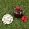 A jar of jam with raspberries and a lid with a strawberry pattern on grass. Produktbild-Vorschau
