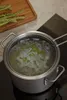 A pot of boiling water with pasta in it sits on a stovetop, with asparagus on a cutting board in the background. Podgląd zdjęcia produktu