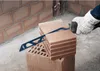 A gloved hand is using a saw to cut a brick, with other bricks and a brick wall in the background. Voir les images du produit