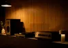 A turntable, amplifier, and speaker are set up on a shelf against a wood-paneled wall, illuminated by a pendant lamp and a small table lamp. Produktbild-Vorschau