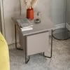 A modern nightstand with books, a vase with dried flowers, and a small decorative object on top, placed next to a yellow sofa and a floor lamp. Produktbild-Vorschau