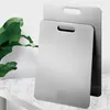 Two stainless steel cutting boards are shown, one in front of the other, with a large green leaf to the left. Produktbild-Vorschau