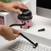 A person is using a small pink vacuum cleaner to clean a computer keyboard. Produktbild-Vorschau